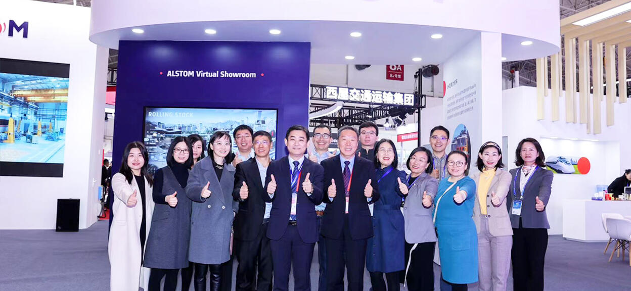 Alstom employees thumbs up in front of Alstom booth at Modern Railways 2023