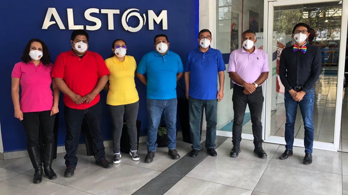 People in rainbow shirts standing in front of Alstom sign