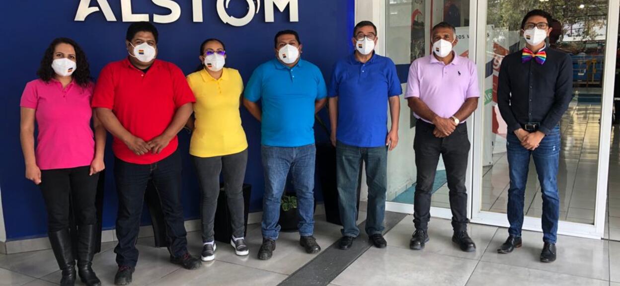 People in rainbow shirts standing in front of Alstom sign