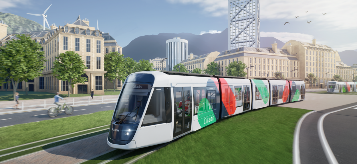 This artist's drawing shows a tram moving from right to left in an urban environment. The tram has a white livery with green, blue and red spots. It bears the Citadis name on its side and on the display above the windscreen. A second tram can be seen in the distance, on the right-hand side. The trams are travelling along a grassy avenue. Buildings can be seen in the background and mountains in the distance.
