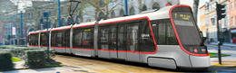 A Citadis tram bearing the logos of Ilevia is shown travelling from left to right along a tree-lined avenue. The train’s display screen shows its destination (Gare de Lille Flandres)