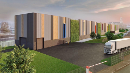 Un grand bâtiment traverse l’image de gauche à droite. Devant le bâtiment, deux personnes discutent sur un parking. Un camion blanc est garé en bas à droite de l’image. On voit des voitures stationnées plus loin et, dans le lointain, une église avec son clocher.