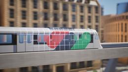 Une image de synthèse présente une rame de train circulant sur un viaduc (de la gauche vers la droite). La rame porte une livrée avec des taches de couleur rouge, verte et bleue, ainsi qu’un quadrillage blanc. L’arrière-plan est flouté. On devine des immeubles de plusieurs étages de couleur ocre.