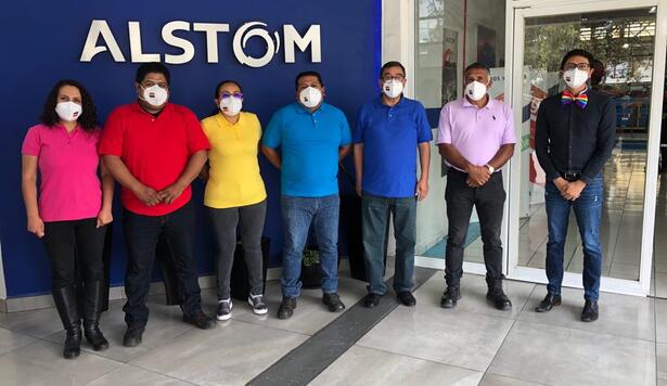 People in rainbow shirts standing in front of Alstom sign
