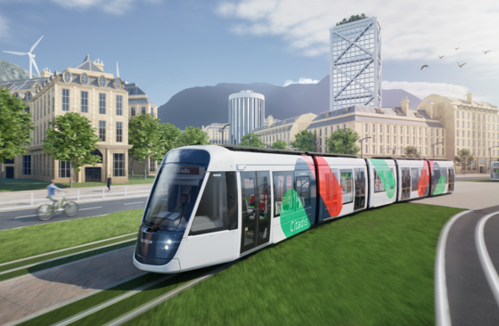 This artist's drawing shows a tram moving from right to left in an urban environment. The tram has a white livery with green, blue and red spots. It bears the Citadis name on its side and on the display above the windscreen. A second tram can be seen in the distance, on the right-hand side. The trams are travelling along a grassy avenue. Buildings can be seen in the background and mountains in the distance.